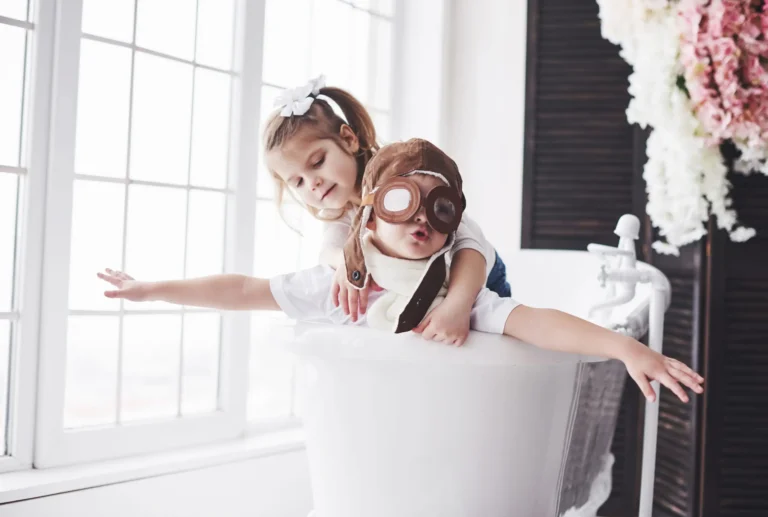 A child wearing a plane pilot costume spreads his arms like wings while sitting in a bathtub